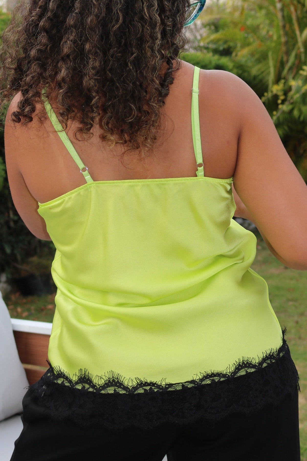 A woman outdoors wearing a bright neon yellow-green spaghetti-strap top with black lace trim at the hem, photographed from behind.